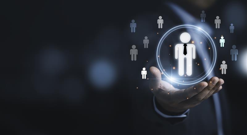 A digitally rendered image of a businessperson’s hand holding a glowing human icon, surrounded by other stylized icons representing people. The image symbolizes HR, talent management, or customer-centric technology solutions.